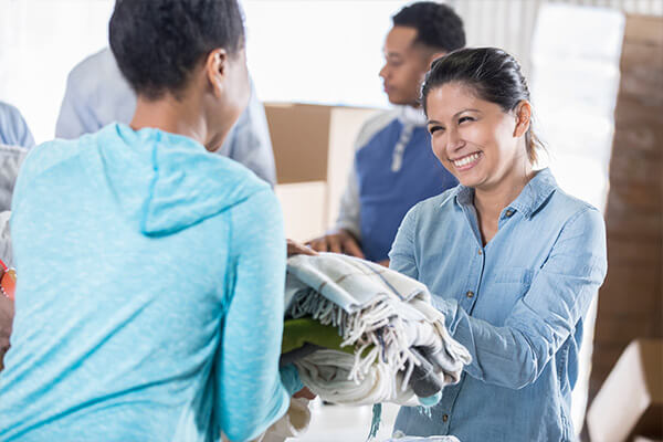 Cheerful mid adult woman hands a warm blanket to a woman in need during a clothing drive.